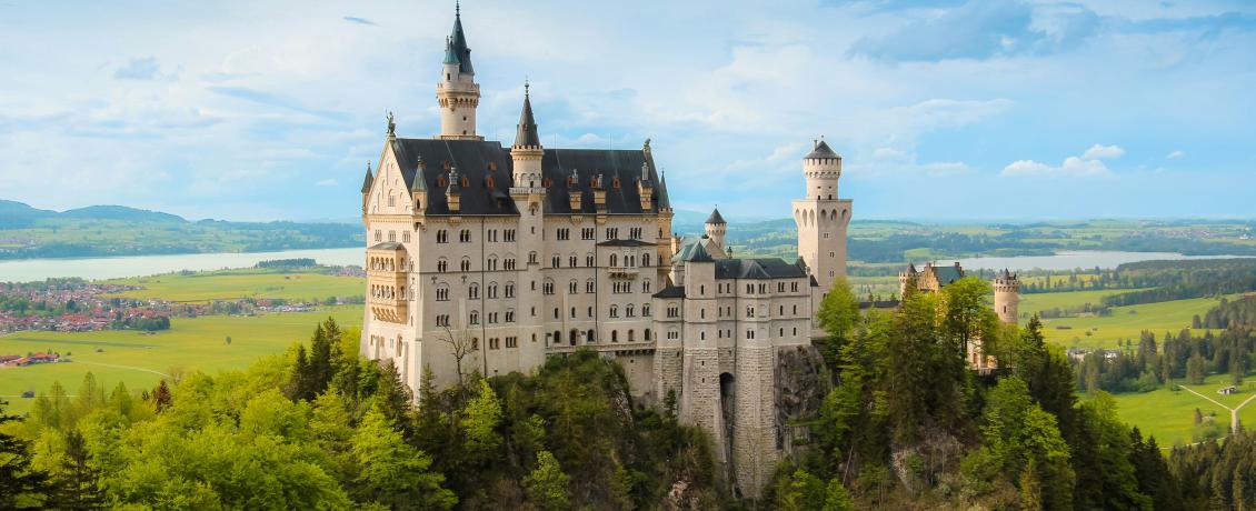 Neuschwanstein Castle surrounded by green forests and fields.