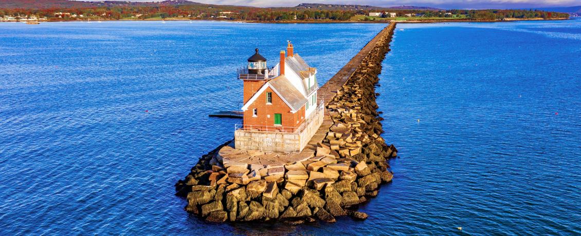 Rockland Breakwater Lighthouse on a stone pier, surrounded by blue waters and hills