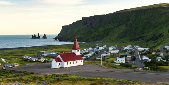 Vík, Iceland, with a red-roofed church and dramatic rock formations in the sea.